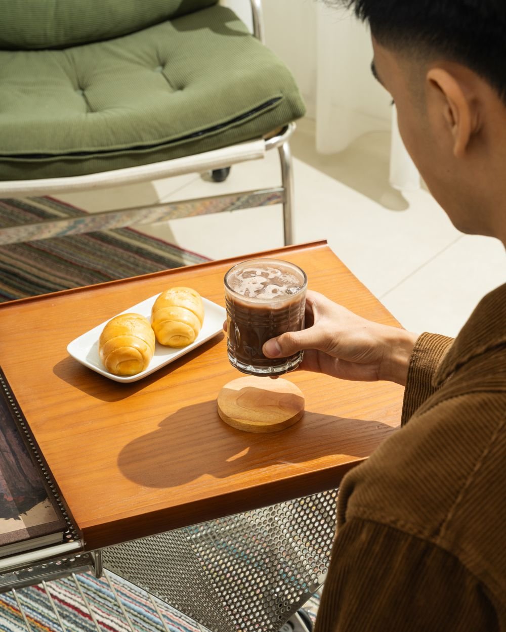 Man holding an iced chocolate drink beside a plate of croissants
